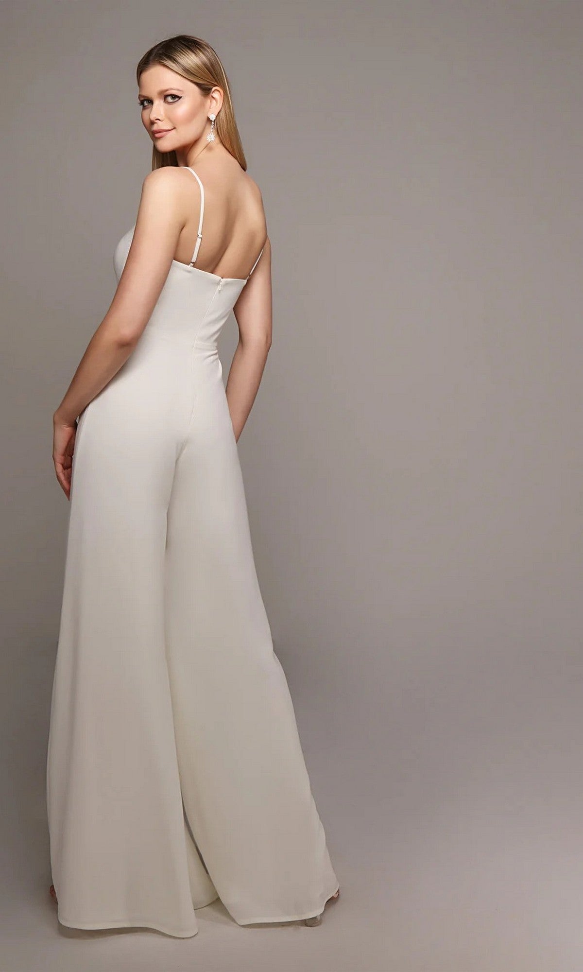 A woman faces away, wearing the Alyce 70022 long white jumpsuit—an ivory sleeveless design with thin straps and wide-leg pants—set against a plain light gray background.
